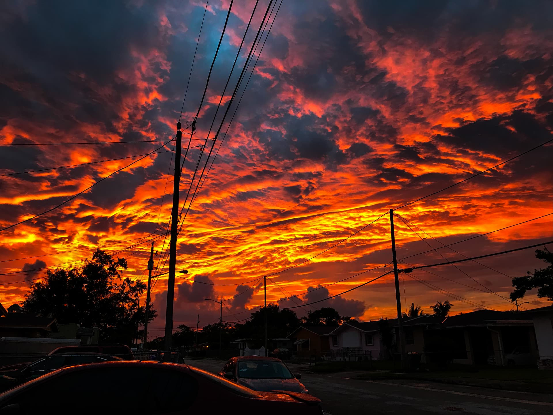Fiery red and orange clouds over a neighborhood street one minute before dark
