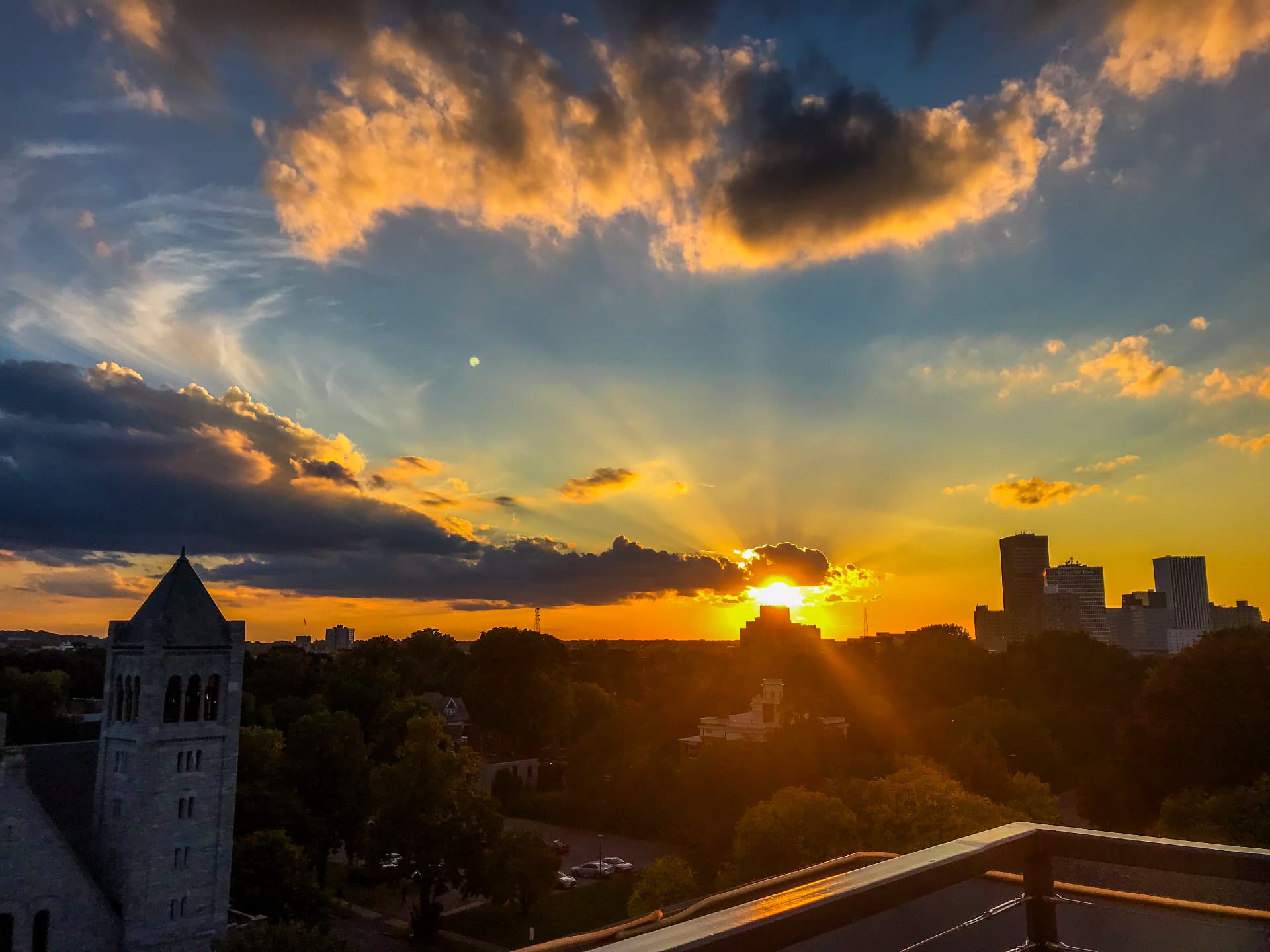 Sun setting behind a city skyline with a stone tower in the foreground
